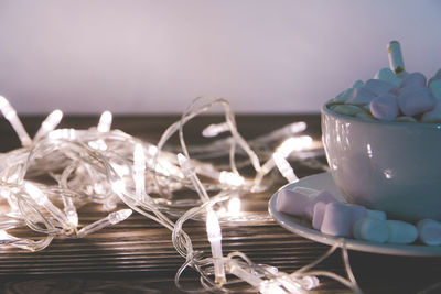 Close-up of marshmallows in cup with christmas lights on table