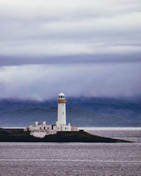 Lighthouse by sea and buildings against sky