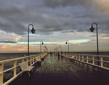 Street lights on footpath by sea against sky