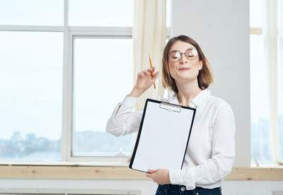 Young woman using phone while standing on window