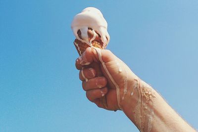 Low angle view of cropped hand against blue sky