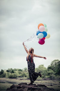 Low angle view of woman holding balloons against sky