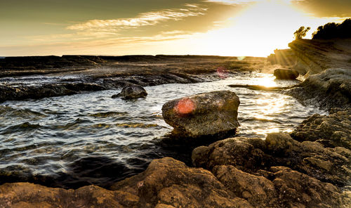 Rocky beach against sky during sunset