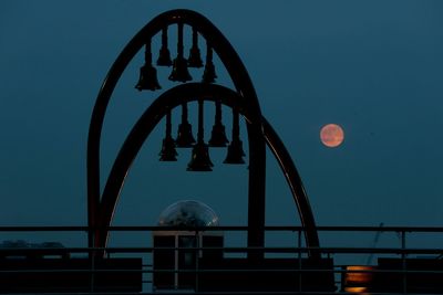 Silhouette bells against moon in sky at night