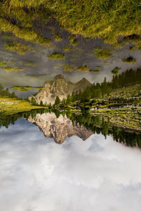 Upside down image of river and mountains against cloudy sky