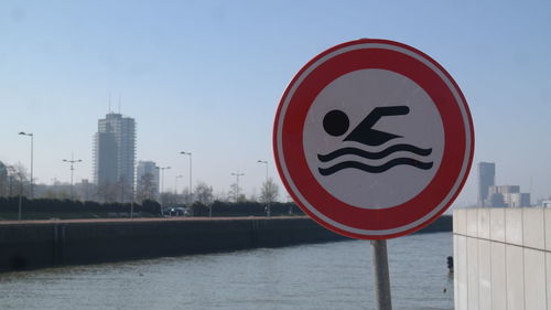 Information sign by river in city against sky