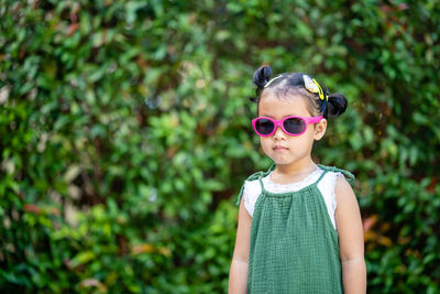 Cute girl wearing sunglasses standing against plants outdoors