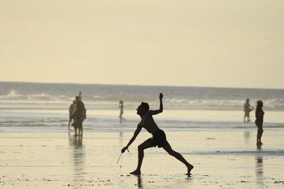 Silhouette man playing on shore at beach against sunset