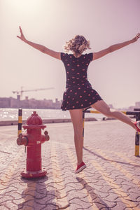 Rear view of happy woman jumping on footpath in city during sunny day