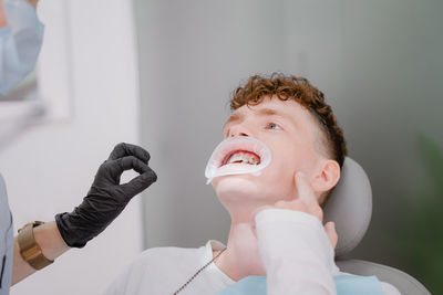 A young guy sitting in a chair at the dentist with braces on his teeth points to the cheek