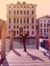 Side view of man photographing while standing on pier by canal in city