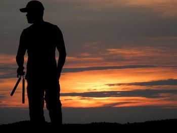 Silhouette man holding nunchaku on field against orange sky