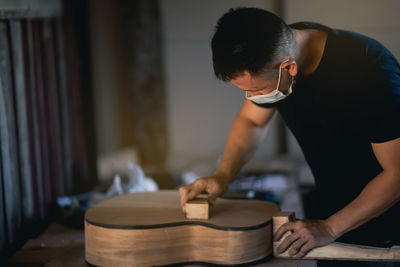 Man wearing mask making guitar at workshop