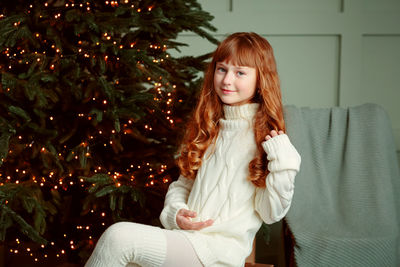 Happy young girl sitting by the christmas tree