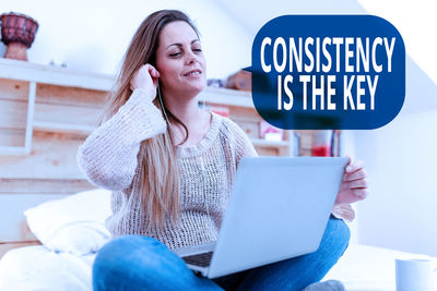 Young woman using mobile phone while sitting on laptop