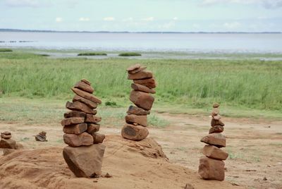 Stack of stones on field by sea against sky