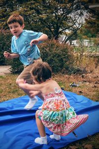 Siblings playing on blue sheet in yard