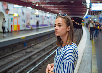Woman looking away while standing at railroad station