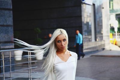 Portrait of young woman standing against building