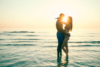 Side view of young couple romancing at beach during sunset