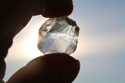 Cropped hand of person holding crystal against sky