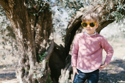 Portrait of boy wearing sunglasses standing against tree