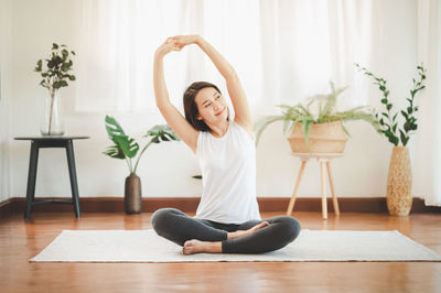 Full length of woman sitting on wooden floor at home