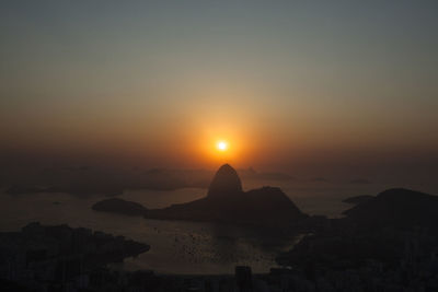 Silhouette city by sea against sky during sunset