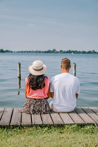 Rear view of couple sitting on shore against sky