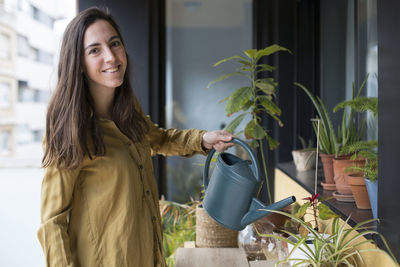 Portrait of smiling young woman standing against potted plants