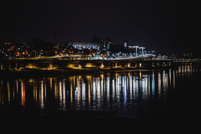 Illuminated buildings by river against sky at night