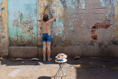 Full length of shirtless man standing against wall