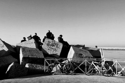 People sitting on land by sea against clear sky