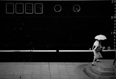 Woman with umbrella walking on steps against moored ship at harbor