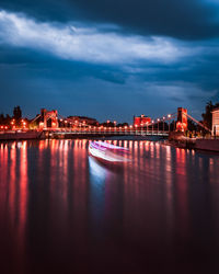 Illuminated bridge over river by buildings against sky at dusk