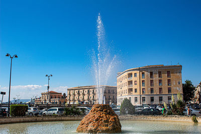 Fountain in city against blue sky