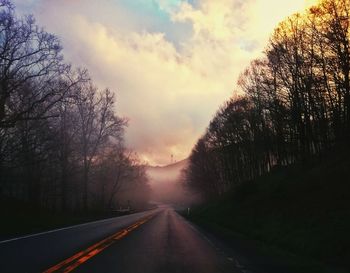 Empty road amidst trees against sky during sunset