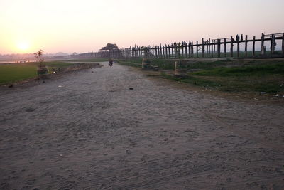 Rear view of woman walking on shore against clear sky during sunset