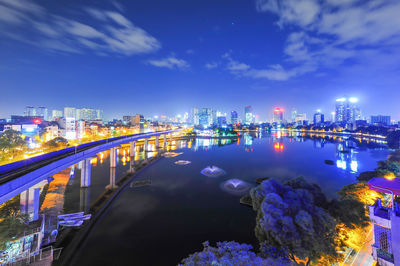 Illuminated buildings by river against sky at night