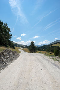 Dirt road along landscape and trees against sky