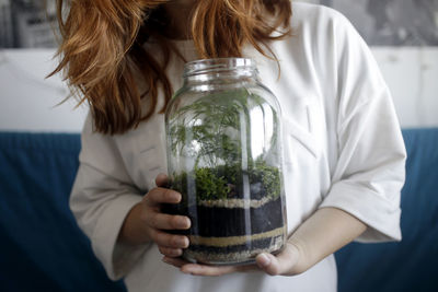 Midsection of young woman carrying plants in container