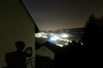 Silhouette man standing by illuminated building against sky at night