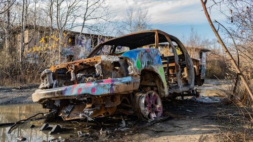 Old abandoned car by bare trees and ruined buildings