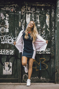 Full length of woman standing against graffiti wall