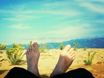 Low section of woman relaxing on beach against sky