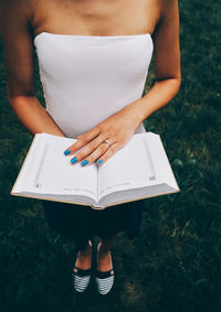 Midsection of woman reading book on field