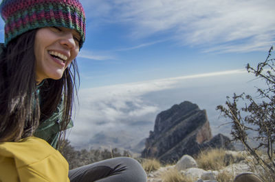 Woman sitting on rock against cloudscape