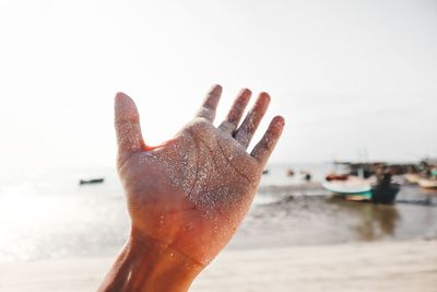 Close-up of messy hand at beach against sky