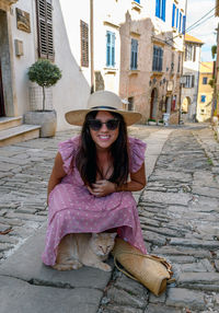 Young woman smiling, ginger cat hiding under dress, street, tourist, town.