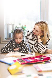 Girl studying while sitting with mother at home